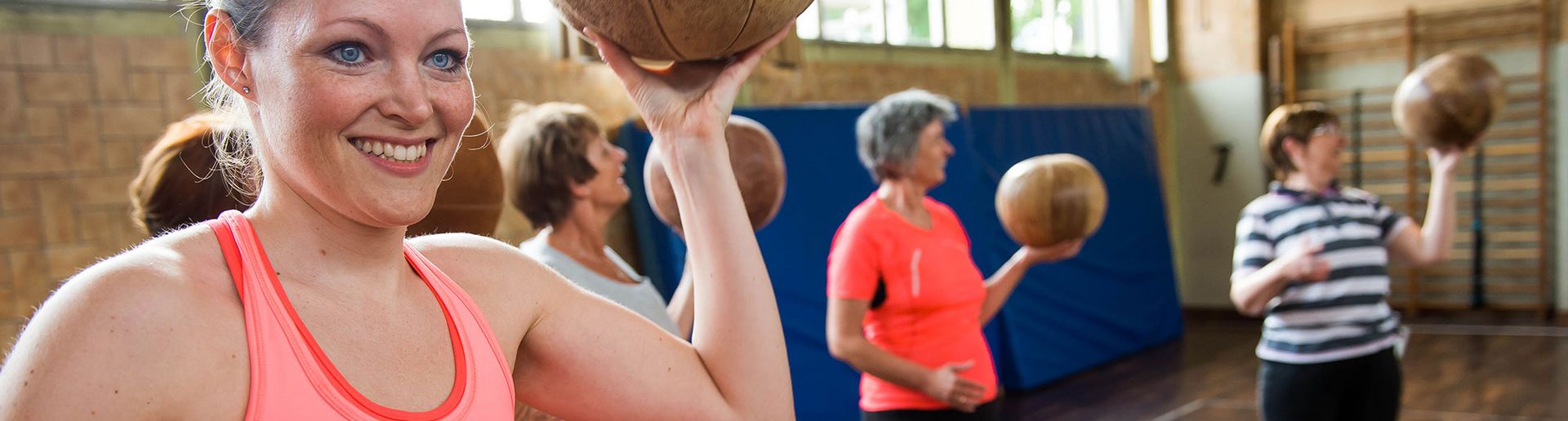 Eien Frau die eine Basketball in der Hand hält, im Hintergrund sieht man noch mehr Fraue, die das gleiche tun