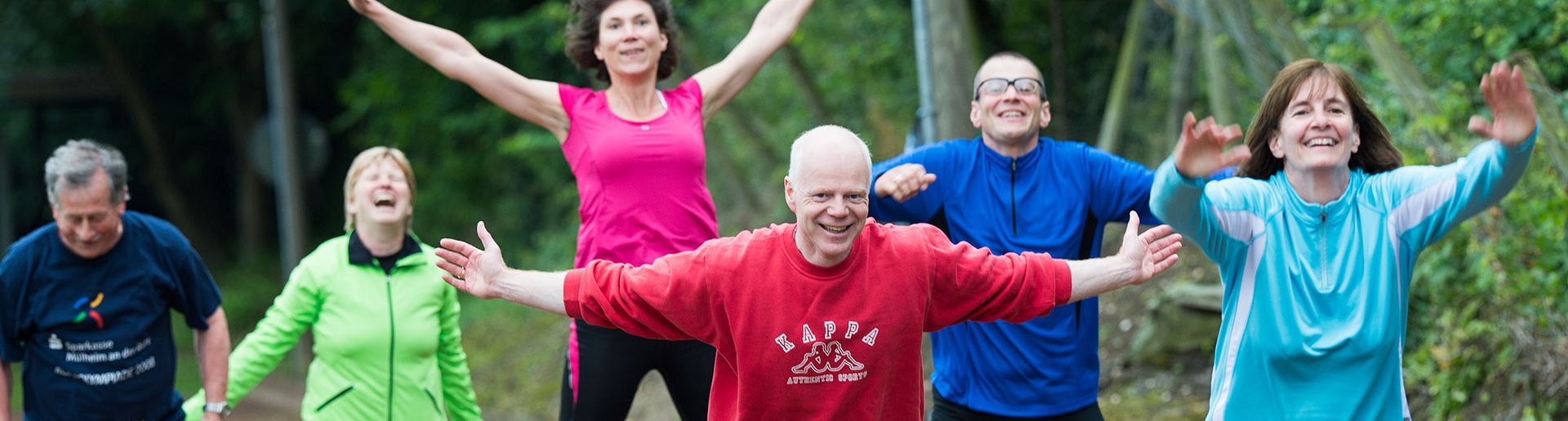 Menschen im Wald, in Sportklamotten, die in die Luft springen und lachen