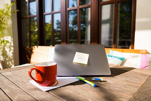 Eine Tasse Kaffe und ein Laptop stehen auf einem Tisch in der Sonne. Auf dem Laptop klebt ein Zetel mit der Aufschrift:"Heute mobil"